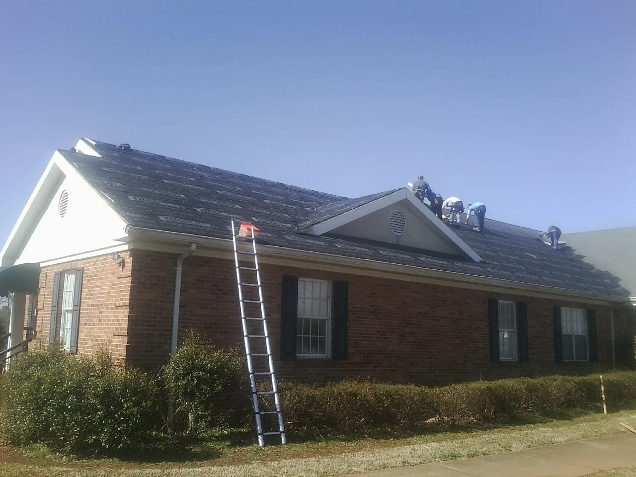 Crew tearing shingles off a brick ranch roof with a ladder set — Metal Roof Repair work by our crew in Satartia