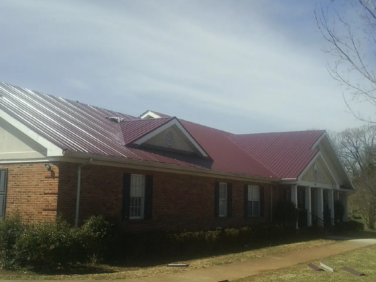Red metal roof with gabled entries on a long brick building, from a Hail Damage Roof Repair job in Satartia