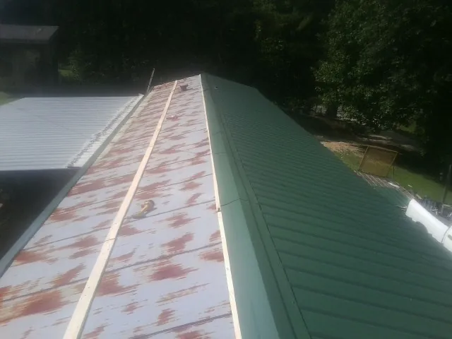 Old rusted panels beside newly installed green metal roofing — Wind Damage Roof Repair by Roofing Brothers in Satartia