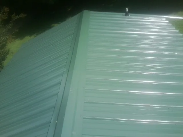 New green metal panels meeting at the ridge of a roof — Flat Roof Repair work by our crew in Satartia