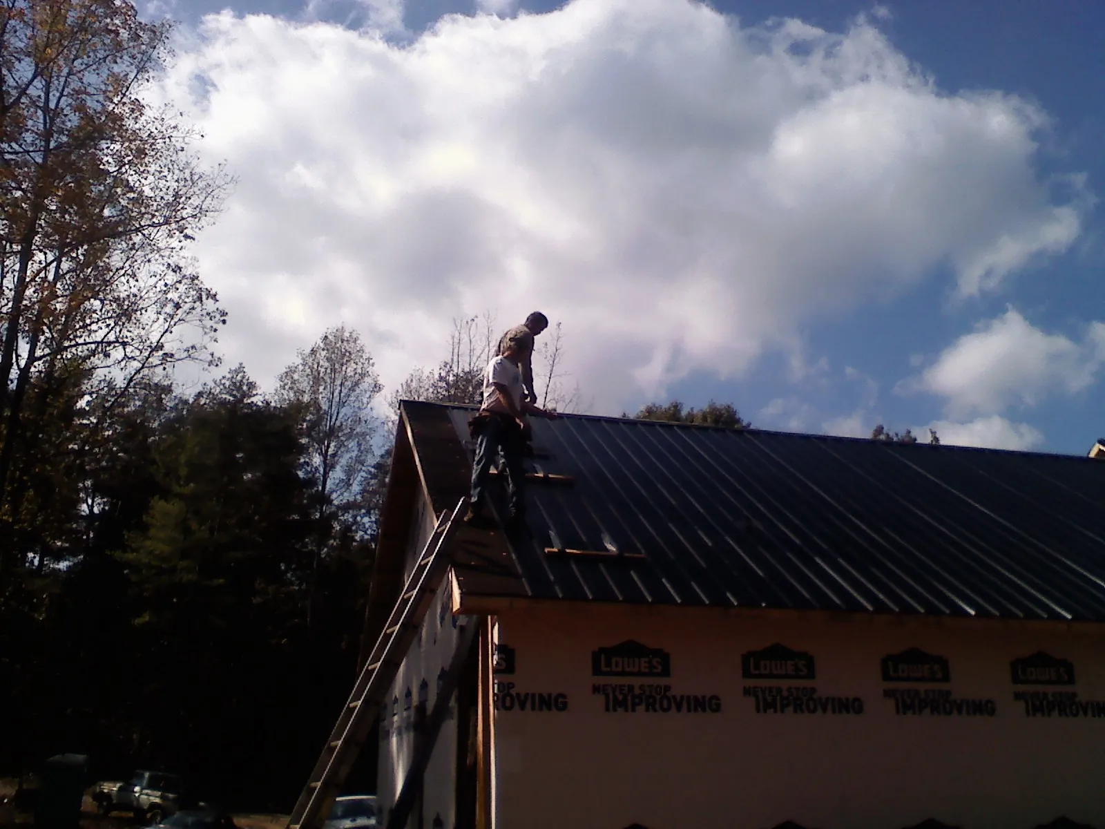 Roofer fastening dark metal panels high against a cloudy sky, from a Roof Inspection job in Satartia