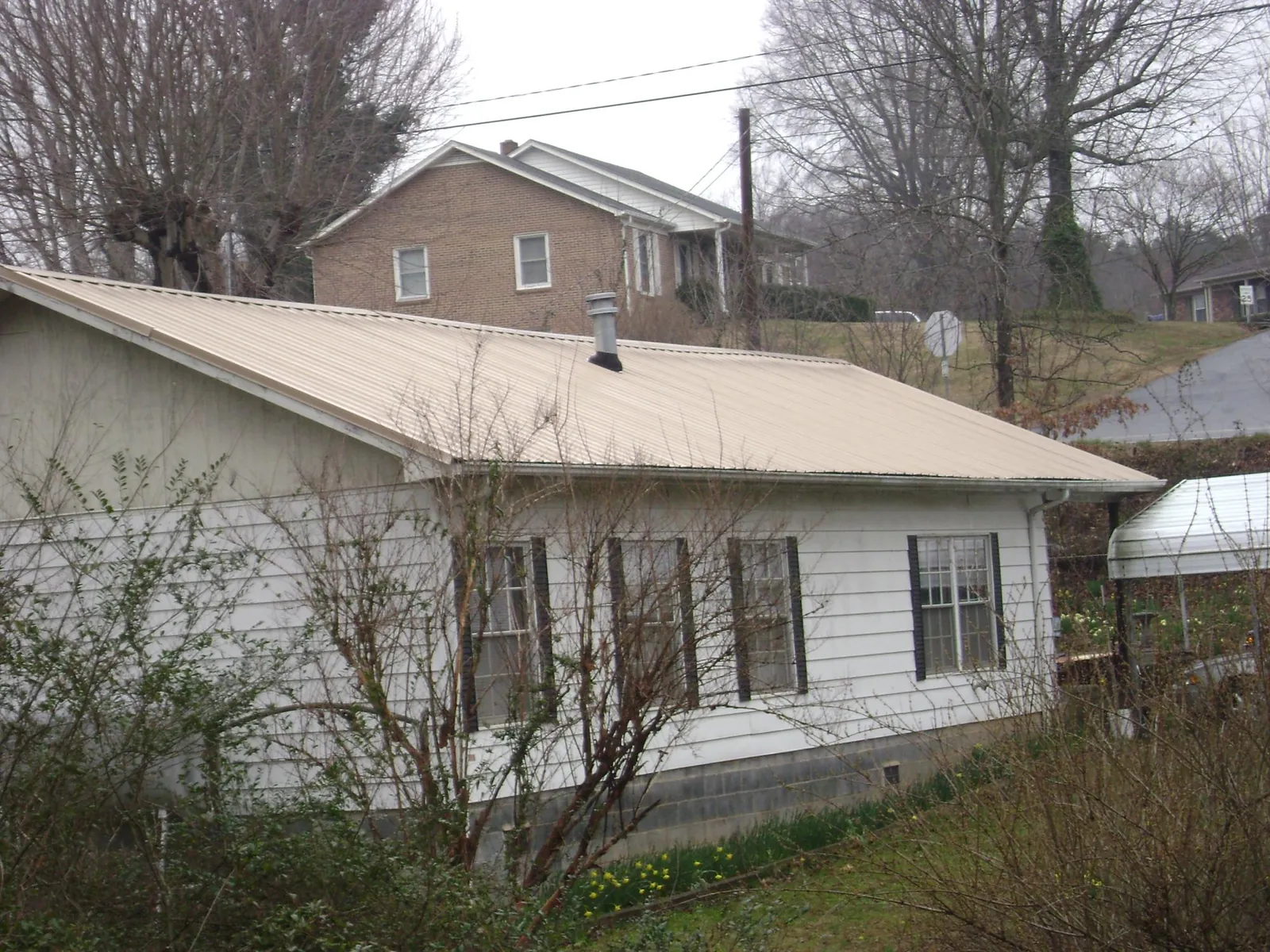 Tan metal roof on a white sided house set into a hillside — Commercial Roofing by Roofing Brothers in Satartia